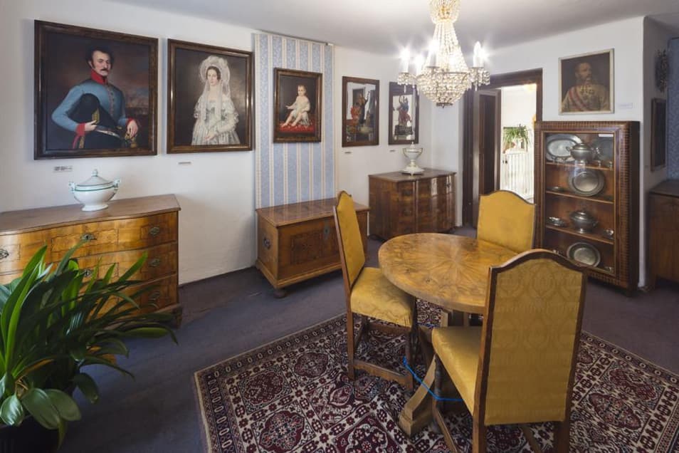 Historischer Innenraum mit Gemälden, Holzmöbeln und Kronleuchter.
