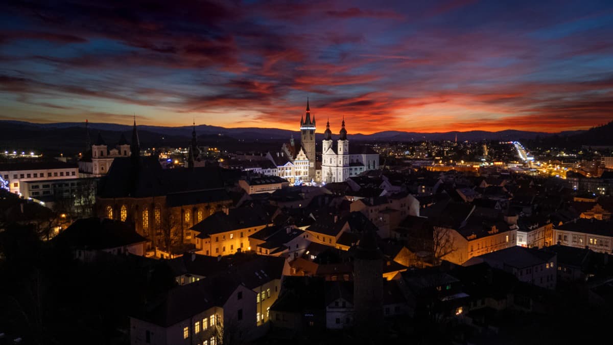 Nachtpanorama einer Stadt mit beleuchteten Gebäuden und dramatischem Himmel.