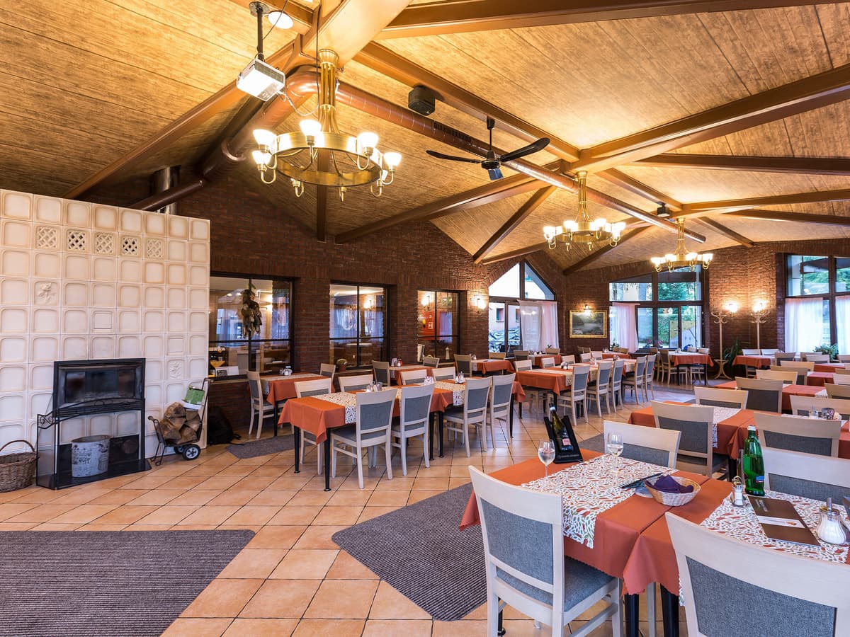 Geräumiges Restaurant mit Holzinterieur, orangefarbenen Tischdecken und großen Fenstern.
