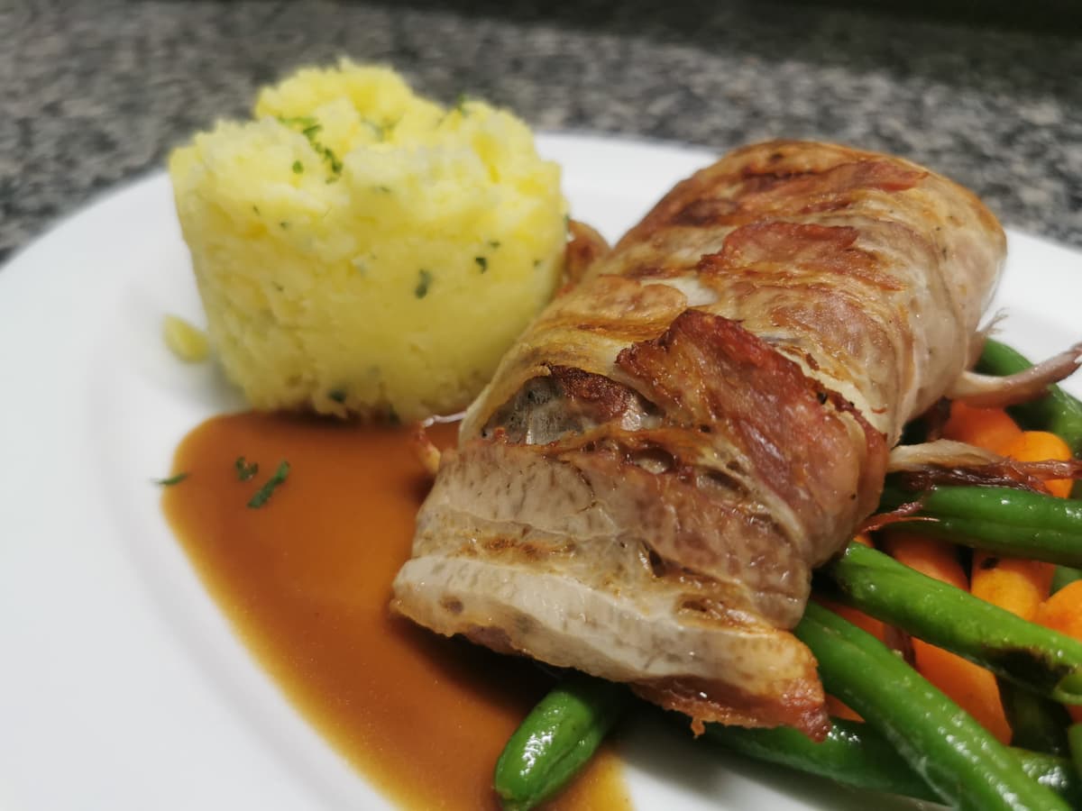 Schweineroulade in Speckscheiben mit Kartoffelpüree und Gemüse.