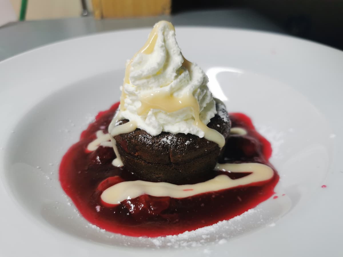 Schokoladenfondant mit Fruchtsauce, Schlagsahne und Beeren.
