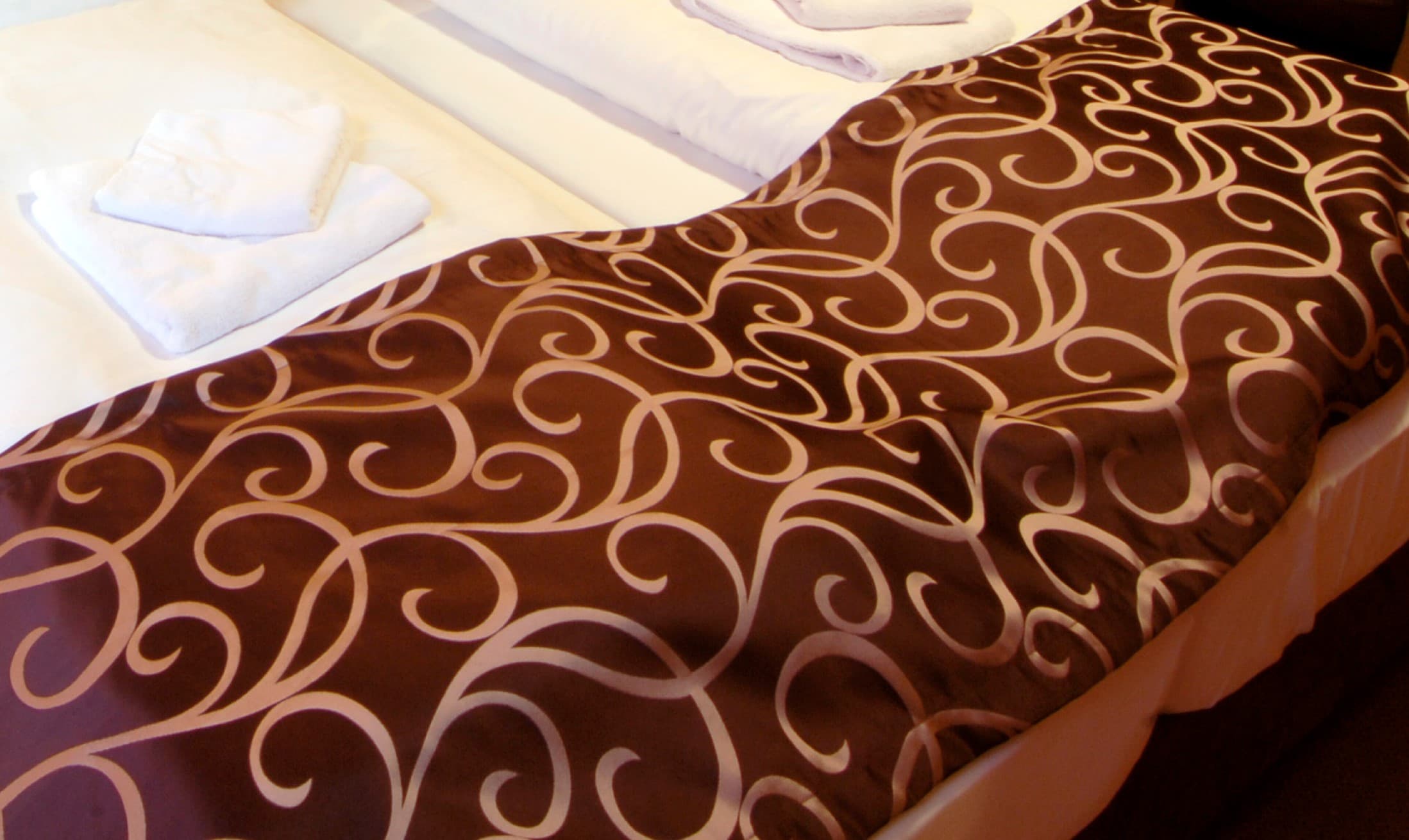 Detail of an elegant bed runner with ornamental pattern and neatly placed towels on the bed