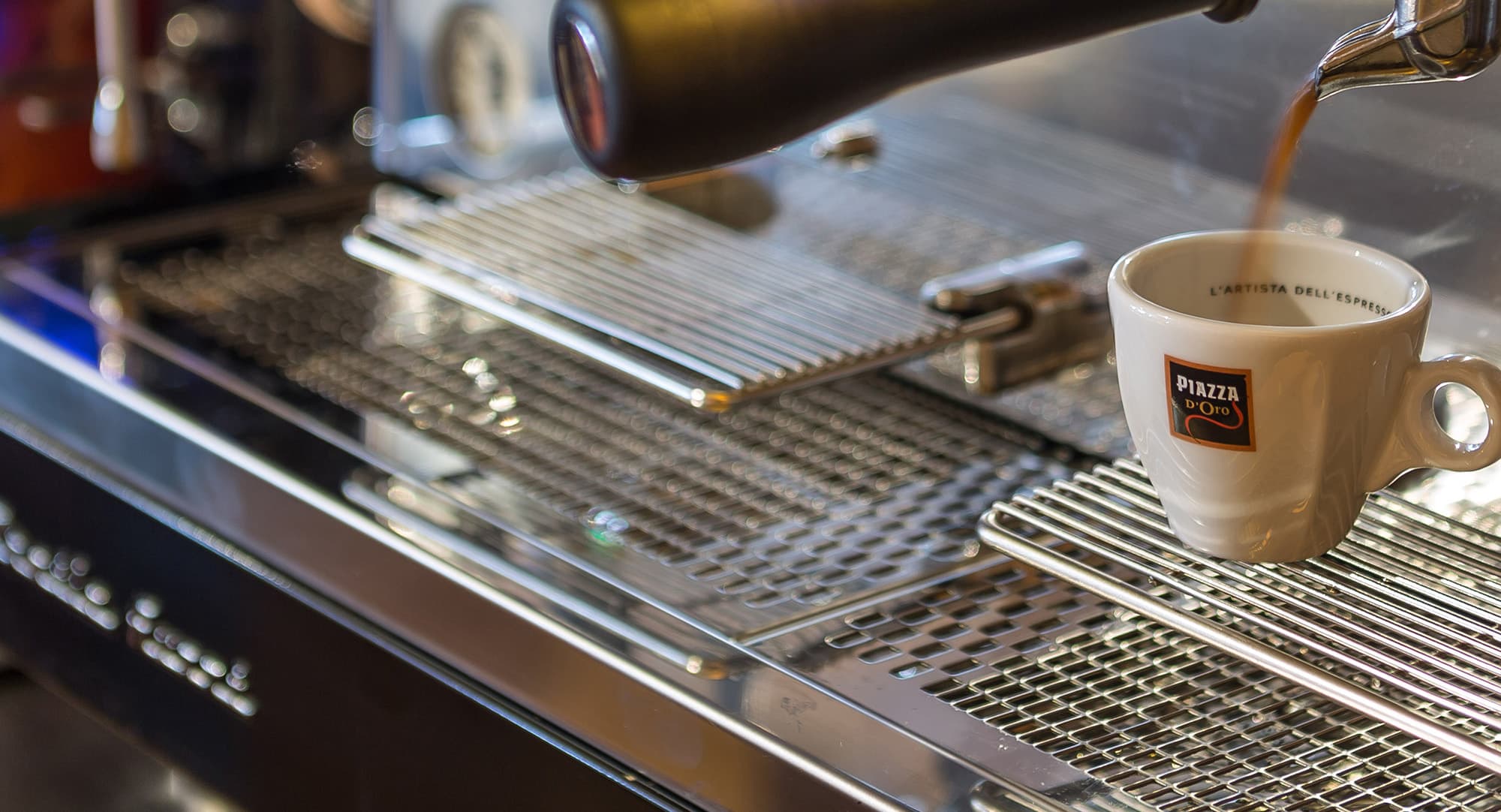 Close-up of a professional espresso machine pouring coffee into a Piazza d’Oro cup