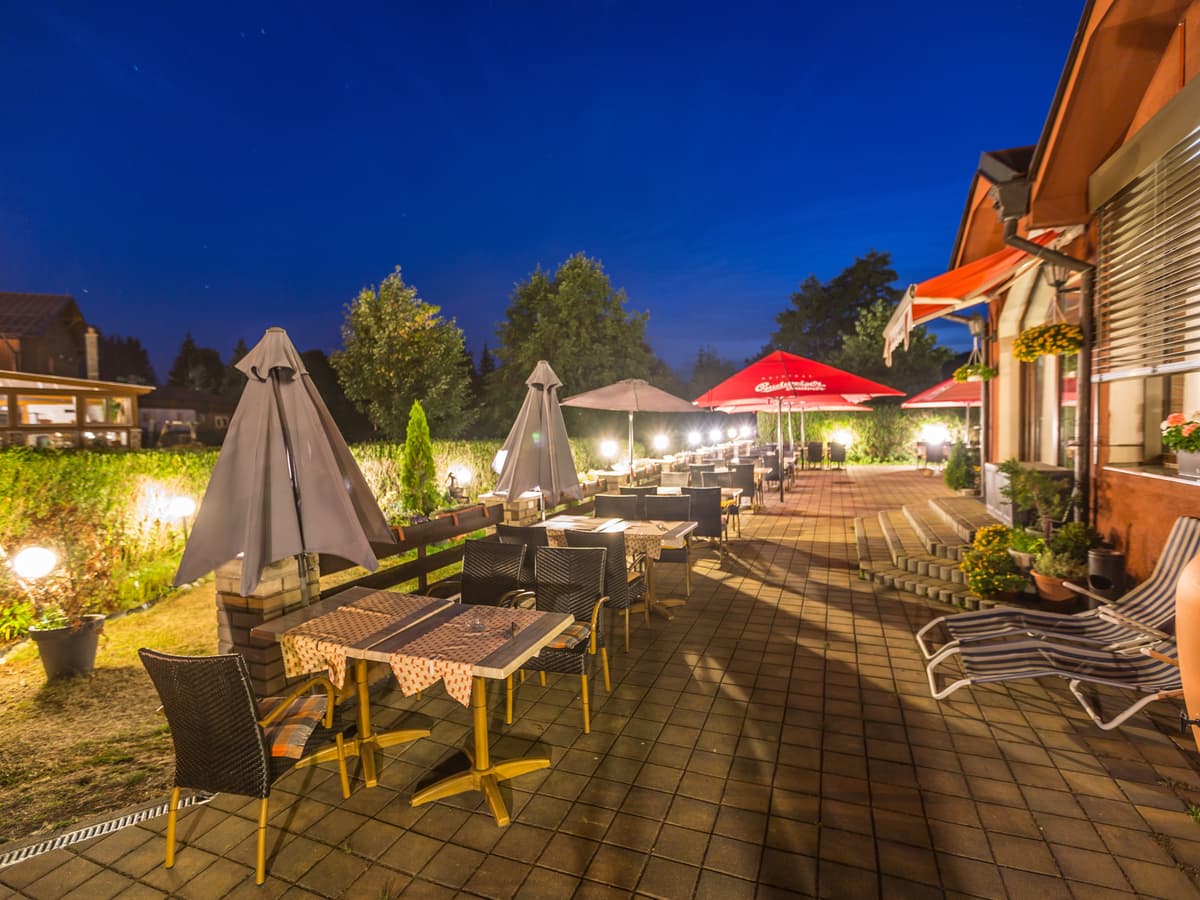 Outdoor terrace with tables, red parasols and lighting at dusk.