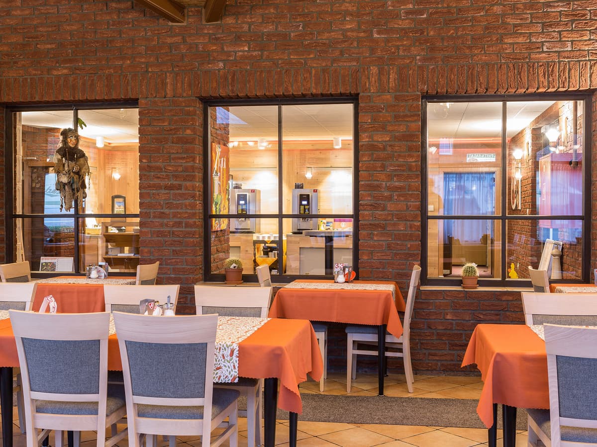 Dining area with brick walls, wooden furniture and orange tablecloths.
